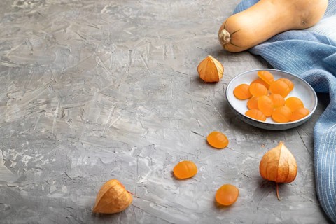 Jelly pumpkin candies on gray concrete background and blue linen textile. copy space, side view.
