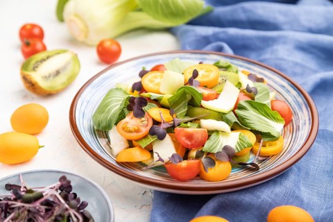 Vegetarian salad of pac choi cabbage, kiwi, tomatoes, kumquat, microgreen sprouts on a white