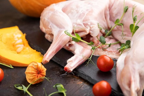 Whole raw rabbit with pumpkin, tomatoes, pea sprouts on a black concrete background and linen