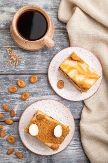 Honey cake with milk cream, caramel, almonds and a cup of coffee on a gray wooden background and