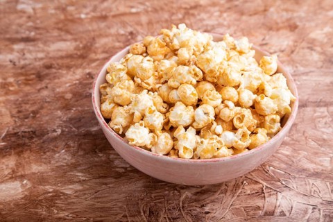 Popcorn with caramel in ceramic bowl on brown concrete background. Side view, close up