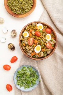 Mung bean porridge with quail eggs, tomatoes and microgreen sprouts on a white wooden background