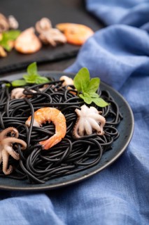 Black cuttlefish ink pasta with shrimps or prawns and small octopuses on black concrete background