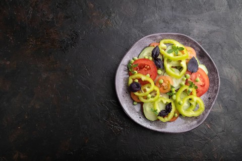 Vegetarian salad from green pea, tomatoes, pepper and basil on a black concrete background. top