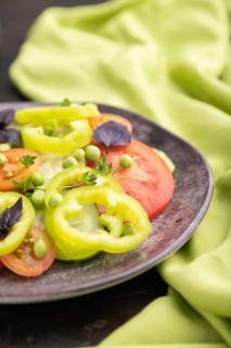 Vegetarian salad from green pea, tomatoes, pepper and basil on a black concrete background and