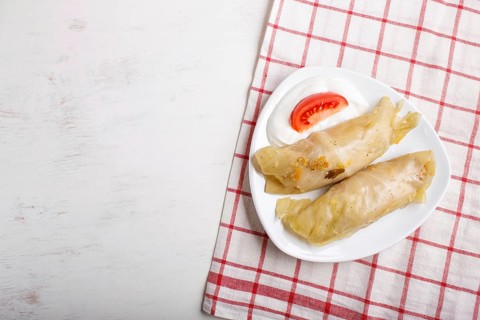 Cabbage rolls with beef, rice and vegetables on a linen tablecloth on a white wooden background.