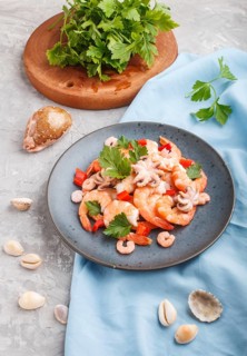 Boiled shrimps or prawns and small octopuses with herbs on a blue ceramic plate on a gray concrete