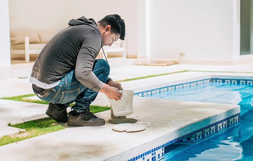 Worker removing trash from swimming pool filter basket. Man cleaning swimming pool garbage filter