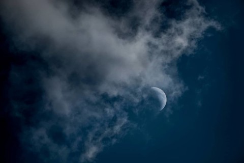 The crescent of the waxing moon in the second quarter shines in a cloudy, dark blue sky,