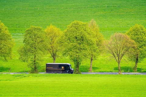 UPS delivery van on a country road, green fields, meadows, trees line the 2-lane road, spring, near