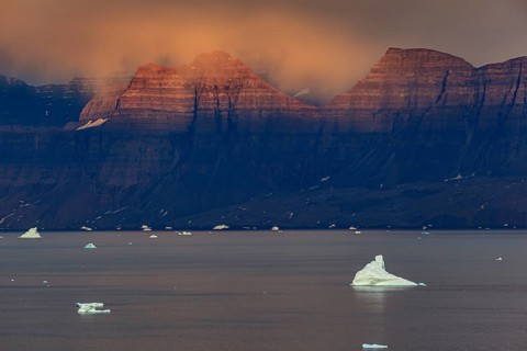 Evening light and atmosphere in fjord with icebergs in front of steep mountains, cloudy, autumn,