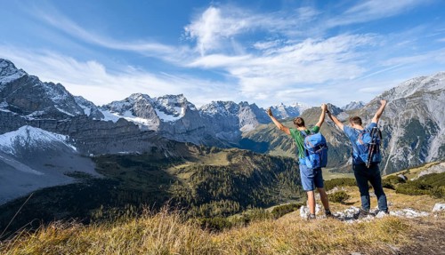 Two mountaineers hand in hand with outstretched arms, on a hiking trail, mountain panorama with
