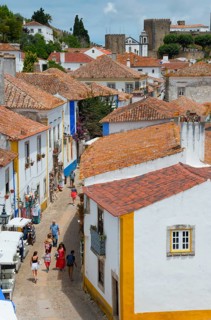 Tourists walk through a cobbled street in the old town with white and yellow facades, view from