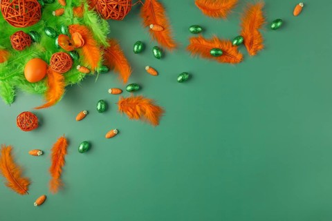 Decorative arrangement with feathers and chocolate eggs in green and orange on a green surface