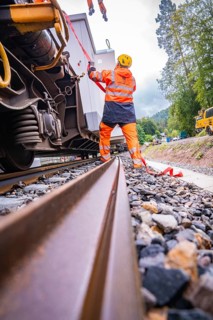 Railway worker in safety clothing works on a railway vehicle and fixes loose parts, surrounded by