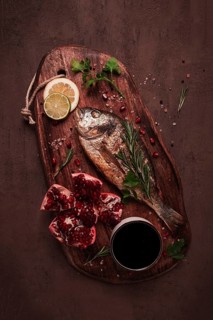 Fried dorado fish, with spices and herbs, on a wooden board, pomegranate sauce, close-up, no people