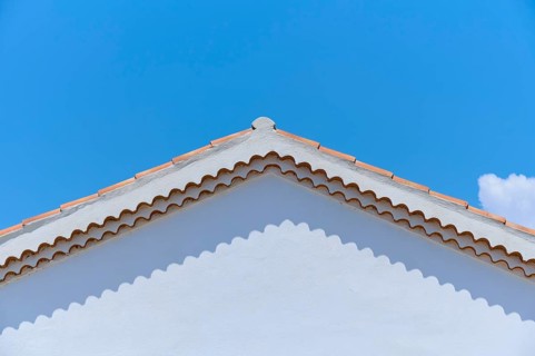 Top of a white painted house with a red tiled roof against a clear blue sky, summer,