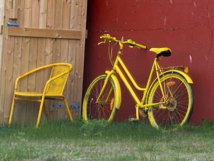A bright yellow bicycle and matching chair placed outdoors by a wooden door and red wall,
