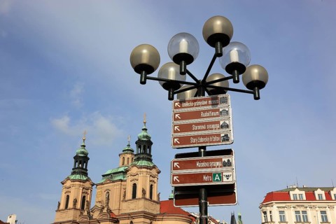 A street lamp on the Old Town Square with signs of the sights in the city and the towers of the