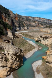 A winding river flows through a rocky gorge in a mountainous landscape under a clear sky, Noguera