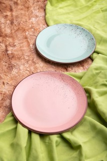 Two empty blue and pink plates on brown concrete background and green textile. Side view, close up