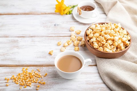 Popcorn with caramel in wooden bowl and a cup of coffee on a white wooden background and linen