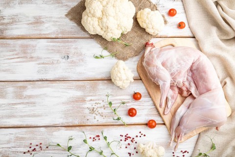 Whole raw rabbit with cauliflower, tomatoes and spices on a white wooden background and linen