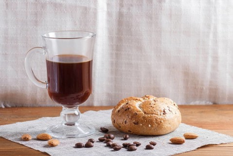 Glass cup of coffee with bun on a wooden background and linen textile. close up, copy space
