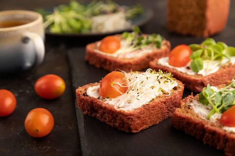 Red beet bread sandwiches with cream cheese, tomatoes and microgreen on black concrete background.