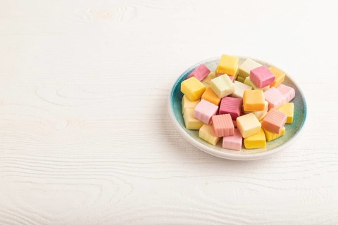 Various fruit jelly chewing candies on plate on white wooden background. apple, banana, tangerine,
