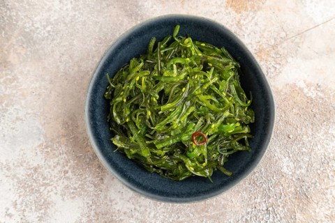 Chuka seaweed salad in blue ceramic bowl on brown concrete background. Top view, flat lay