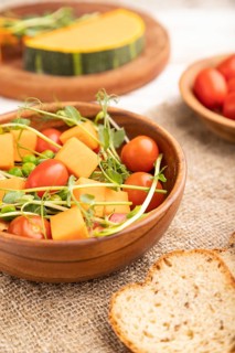 Vegetarian vegetable salad of tomatoes, pumpkin, microgreen pea sprouts on white wooden background