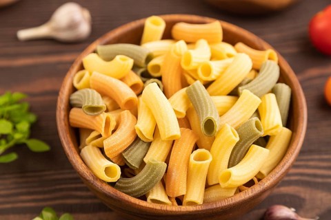 Rigatoni colored raw pasta with tomato, eggs, spices, herbs on brown wooden background. Side view,