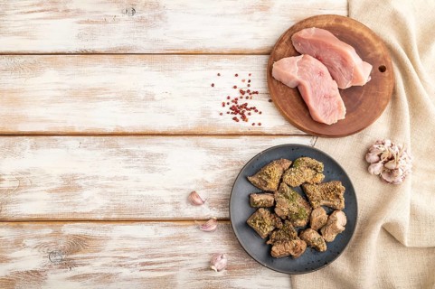 Stewed turkey fillet with garlic on white wooden background and linen textile. Top view, flat lay,