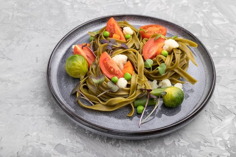 Tagliatelle green spinach pasta with tomato, pea and microgreen sprouts on a gray concrete