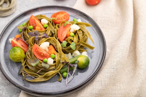 Tagliatelle green spinach pasta with tomato, pea and microgreen sprouts on a gray concrete
