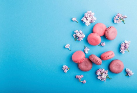 Purple and pink macaron or macaroon cakes with lilac flowers on pastel blue background. Morninig,