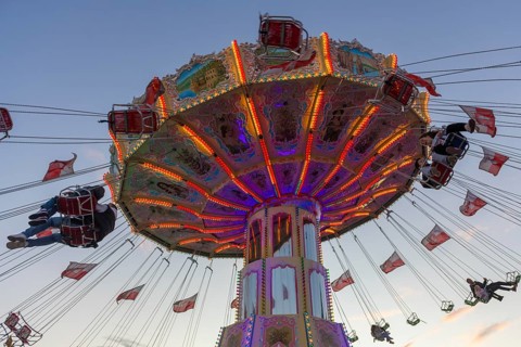 A colourfully illuminated carousel with swinging seats against an evening sky, wave flight, chain