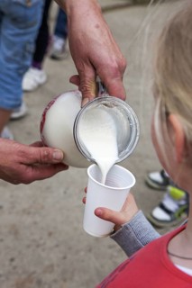 Farmer pouring fresh milk in little girl's plastic cup at farm