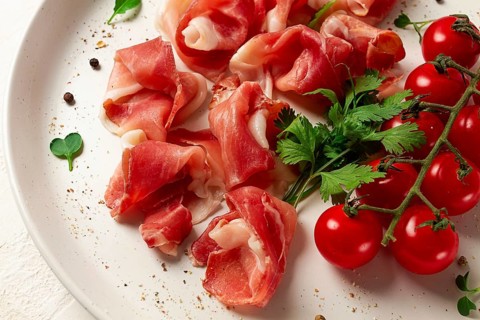 Prosciutto in Scheiben, Vorspeise, mit Kirschtomaten, auf einem weißen Teller, Ansicht von oben