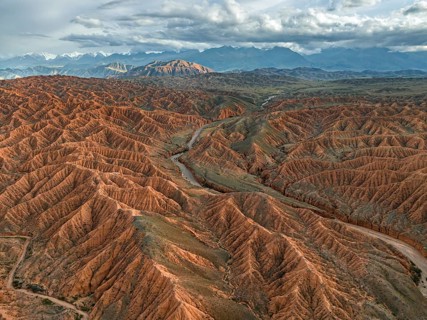 River bed runs through a landscape of eroded hills, badlands at sunset, mountain peaks of the Tian
