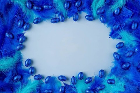 Frame made of blue and turquoise feathers with blue chocolate eggs on a light blue background
