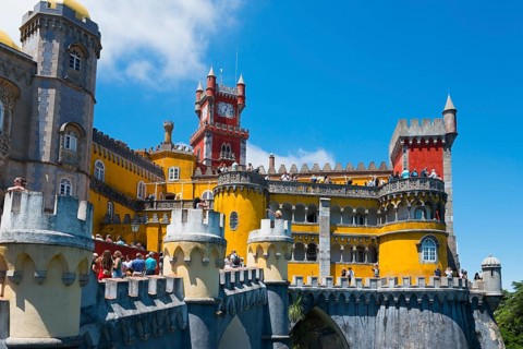 Colourful castle with yellow, red and grey towers, blue sky and visitors, Palácio Nacional da Pena,