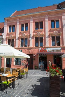 Street view of a pink façade with elaborate stucco details and a café in the foreground, town house