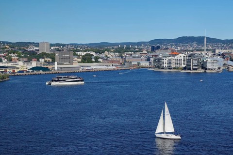 Urban coastal view with a sailing boat, modern harbour and surrounding buildings, electric ferry,