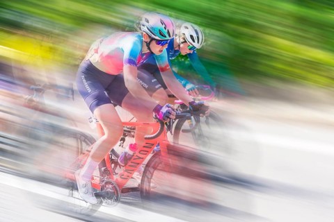 Two female cyclists in sportswear and helmets riding at high speed on a road, racing, the blur of