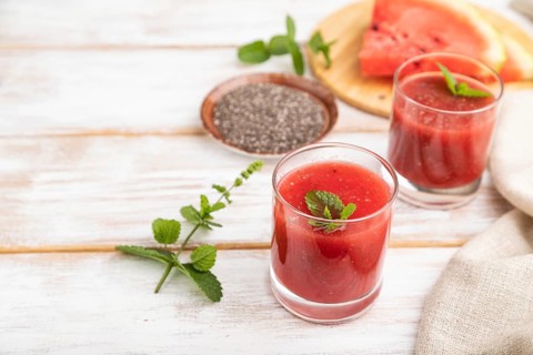 Watermelon juice with chia seeds and mint in glass on a white wooden background with linen textile.