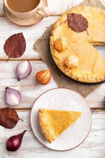 Autumn onion pie decorated with leaves and cup of coffee on white wooden background and linen