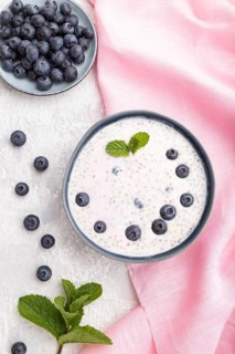 Yogurt with blueberry in ceramic bowl on gray concrete background and pink linen textile. top view,