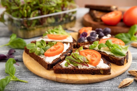 Grain rye bread sandwiches with cream cheese, tomatoes and sorrel microgreen on gray wooden